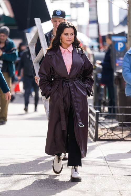 Selena Gomez On The Set in NYC - March 17 2023

Selena Gomez - ''Only Murderers in the Building'' set, NYC - March 17, 2023

Selena Gomez Wears Chic Oversized Plum Coat On 'Only Murders In the Building' Set

On Friday morning, Selena Gomez was photographed on the set of her hit Hulu show Only Murders In The Building in Queens, NY, with her co-stars Steve Martin and Martin Short. The singer and actress' look for the day included black denim pants peeking out from under an oversized dark purple trench coat by Olēnich. The statement piece made from faux leather featured large lapels and a belt cinching her in at the waist.

Under the coat was a pale pink button down and on her feet were a pair of white lace-up boots with a thick black sole.

Gomez left her long brunette hair down in waves and wore a pair of gold double hoop earrings. She had on a natural makeup palette for the shoot with a light coral lip.

On Only Murders in the Building, Gomez plays Mabel Mora, one of a trio of friends who are obsessed with true crime and who start a podcast together as they investigate a murder in their own apartment building. The show was renewed for a third season after receiving much critical acclaim, and has attracted lots of big guest stars like Tina Fey, Ryan Broussard, Jane Lynch, Meryl Streep, Ashley Park, and Paul Rudd.

The pop star told Deadline in an interview last year that when she was pitched the role, she was immediately excited to work with Martin and Short — and that the show's subject was of personal interest to her.

“They pitched me the idea and it led into a whole conversation about my actual obsession with true crime,” said Gomez. “I had just come back from CrimeCon when I had the call and it just felt like it was something I really wanted to do. They were all so lovely. And working with Steve and Marty would be a dream.”

ELLE/AIMÉE LUTKIN