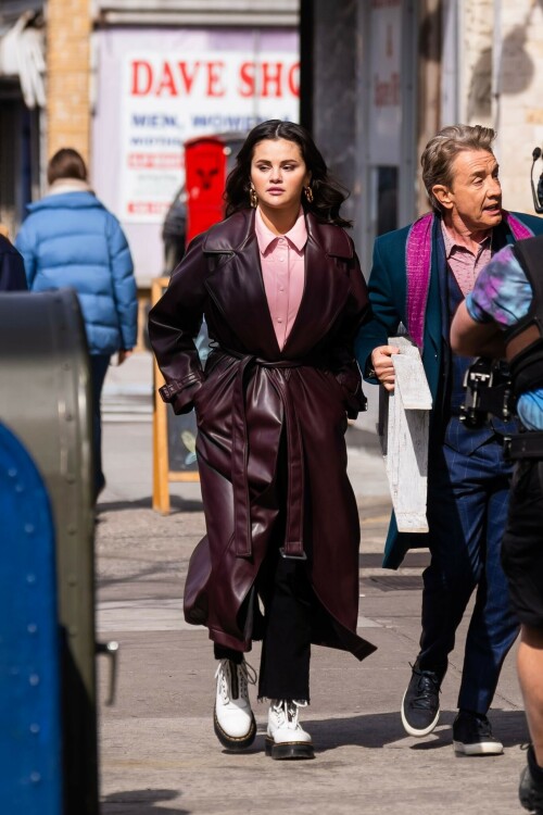 Selena Gomez On The Set in NYC - March 17 2023

Selena Gomez - ''Only Murderers in the Building'' set, NYC - March 17, 2023

Selena Gomez Wears Chic Oversized Plum Coat On 'Only Murders In the Building' Set

On Friday morning, Selena Gomez was photographed on the set of her hit Hulu show Only Murders In The Building in Queens, NY, with her co-stars Steve Martin and Martin Short. The singer and actress' look for the day included black denim pants peeking out from under an oversized dark purple trench coat by Olēnich. The statement piece made from faux leather featured large lapels and a belt cinching her in at the waist.

Under the coat was a pale pink button down and on her feet were a pair of white lace-up boots with a thick black sole.

Gomez left her long brunette hair down in waves and wore a pair of gold double hoop earrings. She had on a natural makeup palette for the shoot with a light coral lip.

On Only Murders in the Building, Gomez plays Mabel Mora, one of a trio of friends who are obsessed with true crime and who start a podcast together as they investigate a murder in their own apartment building. The show was renewed for a third season after receiving much critical acclaim, and has attracted lots of big guest stars like Tina Fey, Ryan Broussard, Jane Lynch, Meryl Streep, Ashley Park, and Paul Rudd.

The pop star told Deadline in an interview last year that when she was pitched the role, she was immediately excited to work with Martin and Short — and that the show's subject was of personal interest to her.

“They pitched me the idea and it led into a whole conversation about my actual obsession with true crime,” said Gomez. “I had just come back from CrimeCon when I had the call and it just felt like it was something I really wanted to do. They were all so lovely. And working with Steve and Marty would be a dream.”

ELLE/AIMÉE LUTKIN