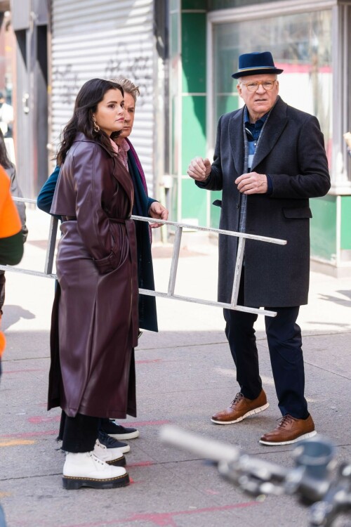 Selena Gomez On The Set in NYC - March 17 2023

Selena Gomez - ''Only Murderers in the Building'' set, NYC - March 17, 2023

Selena Gomez Wears Chic Oversized Plum Coat On 'Only Murders In the Building' Set

On Friday morning, Selena Gomez was photographed on the set of her hit Hulu show Only Murders In The Building in Queens, NY, with her co-stars Steve Martin and Martin Short. The singer and actress' look for the day included black denim pants peeking out from under an oversized dark purple trench coat by Olēnich. The statement piece made from faux leather featured large lapels and a belt cinching her in at the waist.

Under the coat was a pale pink button down and on her feet were a pair of white lace-up boots with a thick black sole.

Gomez left her long brunette hair down in waves and wore a pair of gold double hoop earrings. She had on a natural makeup palette for the shoot with a light coral lip.

On Only Murders in the Building, Gomez plays Mabel Mora, one of a trio of friends who are obsessed with true crime and who start a podcast together as they investigate a murder in their own apartment building. The show was renewed for a third season after receiving much critical acclaim, and has attracted lots of big guest stars like Tina Fey, Ryan Broussard, Jane Lynch, Meryl Streep, Ashley Park, and Paul Rudd.

The pop star told Deadline in an interview last year that when she was pitched the role, she was immediately excited to work with Martin and Short — and that the show's subject was of personal interest to her.

“They pitched me the idea and it led into a whole conversation about my actual obsession with true crime,” said Gomez. “I had just come back from CrimeCon when I had the call and it just felt like it was something I really wanted to do. They were all so lovely. And working with Steve and Marty would be a dream.”

ELLE/AIMÉE LUTKIN