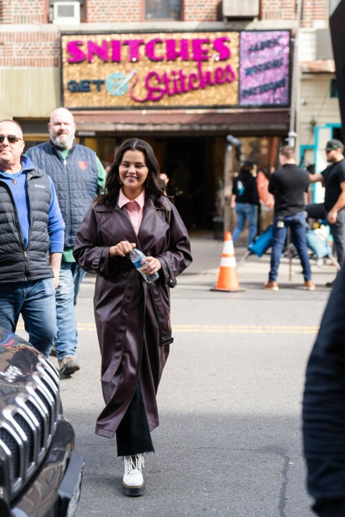 Selena Gomez On The Set in NYC - March 17 2023

Selena Gomez - ''Only Murderers in the Building'' set, NYC - March 17, 2023

Selena Gomez Wears Chic Oversized Plum Coat On 'Only Murders In the Building' Set

On Friday morning, Selena Gomez was photographed on the set of her hit Hulu show Only Murders In The Building in Queens, NY, with her co-stars Steve Martin and Martin Short. The singer and actress' look for the day included black denim pants peeking out from under an oversized dark purple trench coat by Olēnich. The statement piece made from faux leather featured large lapels and a belt cinching her in at the waist.

Under the coat was a pale pink button down and on her feet were a pair of white lace-up boots with a thick black sole.

Gomez left her long brunette hair down in waves and wore a pair of gold double hoop earrings. She had on a natural makeup palette for the shoot with a light coral lip.

On Only Murders in the Building, Gomez plays Mabel Mora, one of a trio of friends who are obsessed with true crime and who start a podcast together as they investigate a murder in their own apartment building. The show was renewed for a third season after receiving much critical acclaim, and has attracted lots of big guest stars like Tina Fey, Ryan Broussard, Jane Lynch, Meryl Streep, Ashley Park, and Paul Rudd.

The pop star told Deadline in an interview last year that when she was pitched the role, she was immediately excited to work with Martin and Short — and that the show's subject was of personal interest to her.

“They pitched me the idea and it led into a whole conversation about my actual obsession with true crime,” said Gomez. “I had just come back from CrimeCon when I had the call and it just felt like it was something I really wanted to do. They were all so lovely. And working with Steve and Marty would be a dream.”

ELLE/AIMÉE LUTKIN