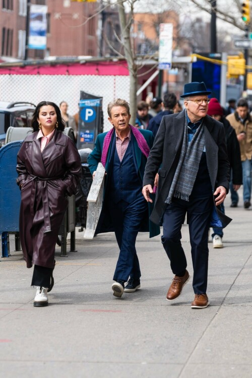 Selena Gomez On The Set in NYC - March 17 2023

Selena Gomez - ''Only Murderers in the Building'' set, NYC - March 17, 2023

Selena Gomez Wears Chic Oversized Plum Coat On 'Only Murders In the Building' Set

On Friday morning, Selena Gomez was photographed on the set of her hit Hulu show Only Murders In The Building in Queens, NY, with her co-stars Steve Martin and Martin Short. The singer and actress' look for the day included black denim pants peeking out from under an oversized dark purple trench coat by Olēnich. The statement piece made from faux leather featured large lapels and a belt cinching her in at the waist.

Under the coat was a pale pink button down and on her feet were a pair of white lace-up boots with a thick black sole.

Gomez left her long brunette hair down in waves and wore a pair of gold double hoop earrings. She had on a natural makeup palette for the shoot with a light coral lip.

On Only Murders in the Building, Gomez plays Mabel Mora, one of a trio of friends who are obsessed with true crime and who start a podcast together as they investigate a murder in their own apartment building. The show was renewed for a third season after receiving much critical acclaim, and has attracted lots of big guest stars like Tina Fey, Ryan Broussard, Jane Lynch, Meryl Streep, Ashley Park, and Paul Rudd.

The pop star told Deadline in an interview last year that when she was pitched the role, she was immediately excited to work with Martin and Short — and that the show's subject was of personal interest to her.

“They pitched me the idea and it led into a whole conversation about my actual obsession with true crime,” said Gomez. “I had just come back from CrimeCon when I had the call and it just felt like it was something I really wanted to do. They were all so lovely. And working with Steve and Marty would be a dream.”

ELLE/AIMÉE LUTKIN