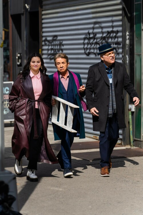 Selena Gomez On The Set in NYC - March 17 2023

Selena Gomez - ''Only Murderers in the Building'' set, NYC - March 17, 2023

Selena Gomez Wears Chic Oversized Plum Coat On 'Only Murders In the Building' Set

On Friday morning, Selena Gomez was photographed on the set of her hit Hulu show Only Murders In The Building in Queens, NY, with her co-stars Steve Martin and Martin Short. The singer and actress' look for the day included black denim pants peeking out from under an oversized dark purple trench coat by Olēnich. The statement piece made from faux leather featured large lapels and a belt cinching her in at the waist.

Under the coat was a pale pink button down and on her feet were a pair of white lace-up boots with a thick black sole.

Gomez left her long brunette hair down in waves and wore a pair of gold double hoop earrings. She had on a natural makeup palette for the shoot with a light coral lip.

On Only Murders in the Building, Gomez plays Mabel Mora, one of a trio of friends who are obsessed with true crime and who start a podcast together as they investigate a murder in their own apartment building. The show was renewed for a third season after receiving much critical acclaim, and has attracted lots of big guest stars like Tina Fey, Ryan Broussard, Jane Lynch, Meryl Streep, Ashley Park, and Paul Rudd.

The pop star told Deadline in an interview last year that when she was pitched the role, she was immediately excited to work with Martin and Short — and that the show's subject was of personal interest to her.

“They pitched me the idea and it led into a whole conversation about my actual obsession with true crime,” said Gomez. “I had just come back from CrimeCon when I had the call and it just felt like it was something I really wanted to do. They were all so lovely. And working with Steve and Marty would be a dream.”

ELLE/AIMÉE LUTKIN