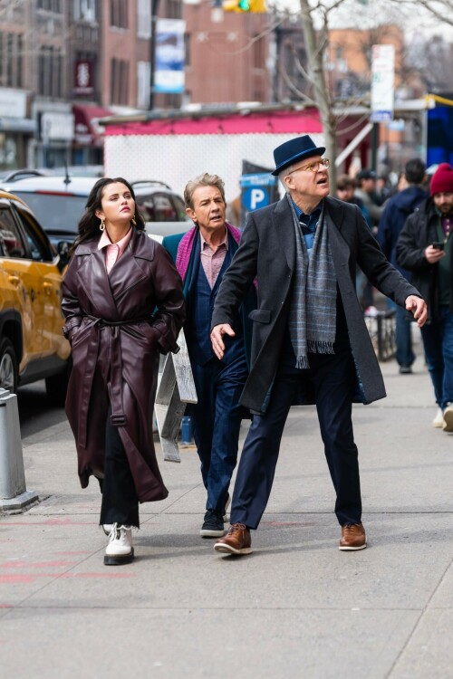 Selena Gomez On The Set in NYC - March 17 2023

Selena Gomez - ''Only Murderers in the Building'' set, NYC - March 17, 2023

Selena Gomez Wears Chic Oversized Plum Coat On 'Only Murders In the Building' Set

On Friday morning, Selena Gomez was photographed on the set of her hit Hulu show Only Murders In The Building in Queens, NY, with her co-stars Steve Martin and Martin Short. The singer and actress' look for the day included black denim pants peeking out from under an oversized dark purple trench coat by Olēnich. The statement piece made from faux leather featured large lapels and a belt cinching her in at the waist.

Under the coat was a pale pink button down and on her feet were a pair of white lace-up boots with a thick black sole.

Gomez left her long brunette hair down in waves and wore a pair of gold double hoop earrings. She had on a natural makeup palette for the shoot with a light coral lip.

On Only Murders in the Building, Gomez plays Mabel Mora, one of a trio of friends who are obsessed with true crime and who start a podcast together as they investigate a murder in their own apartment building. The show was renewed for a third season after receiving much critical acclaim, and has attracted lots of big guest stars like Tina Fey, Ryan Broussard, Jane Lynch, Meryl Streep, Ashley Park, and Paul Rudd.

The pop star told Deadline in an interview last year that when she was pitched the role, she was immediately excited to work with Martin and Short — and that the show's subject was of personal interest to her.

“They pitched me the idea and it led into a whole conversation about my actual obsession with true crime,” said Gomez. “I had just come back from CrimeCon when I had the call and it just felt like it was something I really wanted to do. They were all so lovely. And working with Steve and Marty would be a dream.”

ELLE/AIMÉE LUTKIN