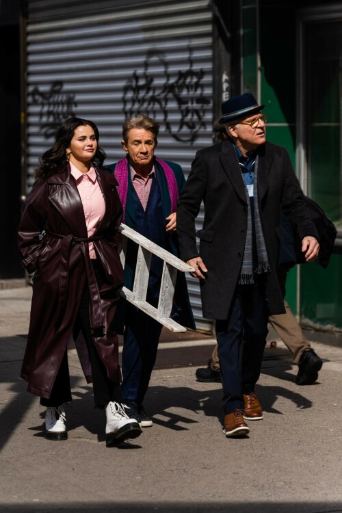 Selena Gomez - ''Only Murderers in the Building'' set, NYC - March 17, 2023

Selena Gomez Wears Chic Oversized Plum Coat On 'Only Murders In the Building' Set

On Friday morning, Selena Gomez was photographed on the set of her hit Hulu show Only Murders In The Building in Queens, NY, with her co-stars Steve Martin and Martin Short. The singer and actress' look for the day included black denim pants peeking out from under an oversized dark purple trench coat by Olēnich. The statement piece made from faux leather featured large lapels and a belt cinching her in at the waist.

Under the coat was a pale pink button down and on her feet were a pair of white lace-up boots with a thick black sole.

Gomez left her long brunette hair down in waves and wore a pair of gold double hoop earrings. She had on a natural makeup palette for the shoot with a light coral lip.

On Only Murders in the Building, Gomez plays Mabel Mora, one of a trio of friends who are obsessed with true crime and who start a podcast together as they investigate a murder in their own apartment building. The show was renewed for a third season after receiving much critical acclaim, and has attracted lots of big guest stars like Tina Fey, Ryan Broussard, Jane Lynch, Meryl Streep, Ashley Park, and Paul Rudd.

The pop star told Deadline in an interview last year that when she was pitched the role, she was immediately excited to work with Martin and Short — and that the show's subject was of personal interest to her.

“They pitched me the idea and it led into a whole conversation about my actual obsession with true crime,” said Gomez. “I had just come back from CrimeCon when I had the call and it just felt like it was something I really wanted to do. They were all so lovely. And working with Steve and Marty would be a dream.”

ELLE/AIMÉE LUTKIN