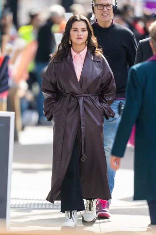 Selena Gomez - ''Only Murderers in the Building'' set, NYC - March 17, 2023

Selena Gomez Wears Chic Oversized Plum Coat On 'Only Murders In the Building' Set

On Friday morning, Selena Gomez was photographed on the set of her hit Hulu show Only Murders In The Building in Queens, NY, with her co-stars Steve Martin and Martin Short. The singer and actress' look for the day included black denim pants peeking out from under an oversized dark purple trench coat by Olēnich. The statement piece made from faux leather featured large lapels and a belt cinching her in at the waist.

Under the coat was a pale pink button down and on her feet were a pair of white lace-up boots with a thick black sole.

Gomez left her long brunette hair down in waves and wore a pair of gold double hoop earrings. She had on a natural makeup palette for the shoot with a light coral lip.

On Only Murders in the Building, Gomez plays Mabel Mora, one of a trio of friends who are obsessed with true crime and who start a podcast together as they investigate a murder in their own apartment building. The show was renewed for a third season after receiving much critical acclaim, and has attracted lots of big guest stars like Tina Fey, Ryan Broussard, Jane Lynch, Meryl Streep, Ashley Park, and Paul Rudd.

The pop star told Deadline in an interview last year that when she was pitched the role, she was immediately excited to work with Martin and Short — and that the show's subject was of personal interest to her.

“They pitched me the idea and it led into a whole conversation about my actual obsession with true crime,” said Gomez. “I had just come back from CrimeCon when I had the call and it just felt like it was something I really wanted to do. They were all so lovely. And working with Steve and Marty would be a dream.”

ELLE/AIMÉE LUTKIN