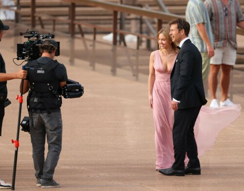 Sydney Sweeney with Glen Powell filming scenes for their upcoming untitled film in Sydney, Australia - March 27 2023

Sydney Sweeney Embraces Rom-Com Dressing in Flowy Pink Dress & Sparkling Sandals While Filming With Glen Powell in Australia

Sydney Sweeney was seen on Monday at the steps of the Sydney Opera House in Sydney, filming for her unnamed upcoming rom-com alongside leading man Glen Powell.

Sweeney and Powell were seen on the steps of the well-known performance center in rom-com-ready ensembles. Powell, who has previously starred in romantic features like “Set It Up,” wore a classic black-and-white tuxedo with black leather point-toe oxfords.

Whereas Sweeney looked every bit the leading lady in a flowing, deeply-cut, deftly-wrapped pink gown with a gauzy overlay of fabric over the skirt. The actress wore her well-known blond locks in a center part and styled them into soft, romantic waves.

For shoes, Sweeney donned a pair of peep-toe silver stiletto heels. The style featured a glittery finish and a ankle-strap for extra security.

When she’s not on set, Sweeney can be seen rocking a variety of footwear styles from ladylike mules to sky-high stilettos. She has been seen wearing a variety of designers, from Jimmy Choo to Tory Burch. Sweeney has been a Tory Burch brand ambassador since Apr. 2022, notably starring in the designer’s summer 2022 campaign, highlighting her popular Miller sandal line.

Sweeney has gained worldwide recognition after playing the love-obsessed Cassie on the hit HBO series “Euphoria”, and in the past year has been stepping into a variety of roles outside of the dramatic high school archetype.

On Jan. 11, Deadline reported that Sweeney and Powell signed on to star in a to-be-named rated-R romantic comedy film directed by Will Gluck. Not only is Sweeney the leading lady of the film, but she is also serving as the project’s executive producer.