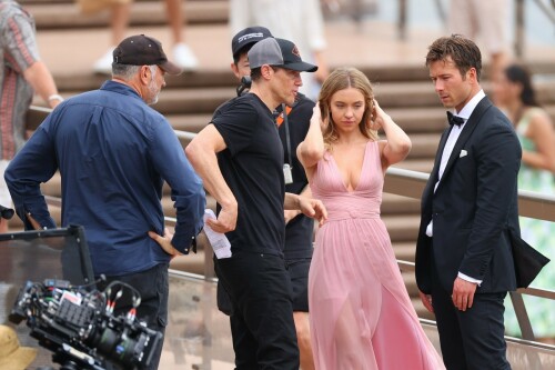 Sydney Sweeney with Glen Powell filming scenes for their upcoming untitled film in Sydney, Australia - March 27 2023

Sydney Sweeney Embraces Rom-Com Dressing in Flowy Pink Dress & Sparkling Sandals While Filming With Glen Powell in Australia

Sydney Sweeney was seen on Monday at the steps of the Sydney Opera House in Sydney, filming for her unnamed upcoming rom-com alongside leading man Glen Powell.

Sweeney and Powell were seen on the steps of the well-known performance center in rom-com-ready ensembles. Powell, who has previously starred in romantic features like “Set It Up,” wore a classic black-and-white tuxedo with black leather point-toe oxfords.

Whereas Sweeney looked every bit the leading lady in a flowing, deeply-cut, deftly-wrapped pink gown with a gauzy overlay of fabric over the skirt. The actress wore her well-known blond locks in a center part and styled them into soft, romantic waves.

For shoes, Sweeney donned a pair of peep-toe silver stiletto heels. The style featured a glittery finish and a ankle-strap for extra security.

When she’s not on set, Sweeney can be seen rocking a variety of footwear styles from ladylike mules to sky-high stilettos. She has been seen wearing a variety of designers, from Jimmy Choo to Tory Burch. Sweeney has been a Tory Burch brand ambassador since Apr. 2022, notably starring in the designer’s summer 2022 campaign, highlighting her popular Miller sandal line.

Sweeney has gained worldwide recognition after playing the love-obsessed Cassie on the hit HBO series “Euphoria”, and in the past year has been stepping into a variety of roles outside of the dramatic high school archetype.

On Jan. 11, Deadline reported that Sweeney and Powell signed on to star in a to-be-named rated-R romantic comedy film directed by Will Gluck. Not only is Sweeney the leading lady of the film, but she is also serving as the project’s executive producer.