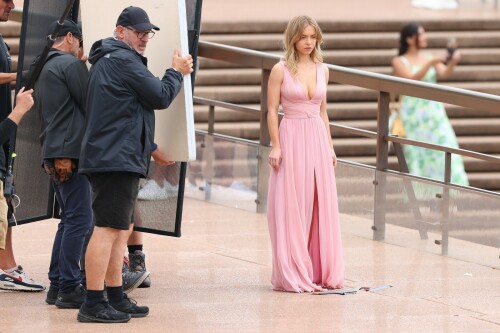 Sydney Sweeney with Glen Powell filming scenes for their upcoming untitled film in Sydney, Australia - March 27 2023

Sydney Sweeney Embraces Rom-Com Dressing in Flowy Pink Dress & Sparkling Sandals While Filming With Glen Powell in Australia

Sydney Sweeney was seen on Monday at the steps of the Sydney Opera House in Sydney, filming for her unnamed upcoming rom-com alongside leading man Glen Powell.

Sweeney and Powell were seen on the steps of the well-known performance center in rom-com-ready ensembles. Powell, who has previously starred in romantic features like “Set It Up,” wore a classic black-and-white tuxedo with black leather point-toe oxfords.

Whereas Sweeney looked every bit the leading lady in a flowing, deeply-cut, deftly-wrapped pink gown with a gauzy overlay of fabric over the skirt. The actress wore her well-known blond locks in a center part and styled them into soft, romantic waves.

For shoes, Sweeney donned a pair of peep-toe silver stiletto heels. The style featured a glittery finish and a ankle-strap for extra security.

When she’s not on set, Sweeney can be seen rocking a variety of footwear styles from ladylike mules to sky-high stilettos. She has been seen wearing a variety of designers, from Jimmy Choo to Tory Burch. Sweeney has been a Tory Burch brand ambassador since Apr. 2022, notably starring in the designer’s summer 2022 campaign, highlighting her popular Miller sandal line.

Sweeney has gained worldwide recognition after playing the love-obsessed Cassie on the hit HBO series “Euphoria”, and in the past year has been stepping into a variety of roles outside of the dramatic high school archetype.

On Jan. 11, Deadline reported that Sweeney and Powell signed on to star in a to-be-named rated-R romantic comedy film directed by Will Gluck. Not only is Sweeney the leading lady of the film, but she is also serving as the project’s executive producer.