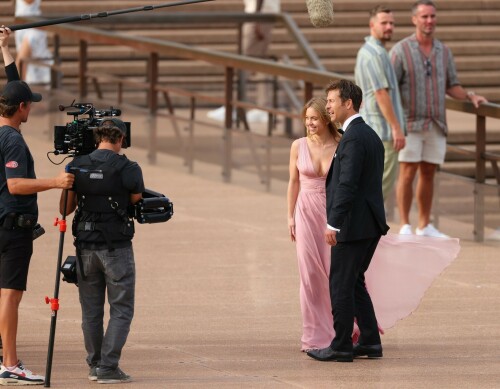 Sydney Sweeney with Glen Powell filming scenes for their upcoming untitled film in Sydney, Australia - March 27 2023

Sydney Sweeney Embraces Rom-Com Dressing in Flowy Pink Dress & Sparkling Sandals While Filming With Glen Powell in Australia

Sydney Sweeney was seen on Monday at the steps of the Sydney Opera House in Sydney, filming for her unnamed upcoming rom-com alongside leading man Glen Powell.

Sweeney and Powell were seen on the steps of the well-known performance center in rom-com-ready ensembles. Powell, who has previously starred in romantic features like “Set It Up,” wore a classic black-and-white tuxedo with black leather point-toe oxfords.

Whereas Sweeney looked every bit the leading lady in a flowing, deeply-cut, deftly-wrapped pink gown with a gauzy overlay of fabric over the skirt. The actress wore her well-known blond locks in a center part and styled them into soft, romantic waves.

For shoes, Sweeney donned a pair of peep-toe silver stiletto heels. The style featured a glittery finish and a ankle-strap for extra security.

When she’s not on set, Sweeney can be seen rocking a variety of footwear styles from ladylike mules to sky-high stilettos. She has been seen wearing a variety of designers, from Jimmy Choo to Tory Burch. Sweeney has been a Tory Burch brand ambassador since Apr. 2022, notably starring in the designer’s summer 2022 campaign, highlighting her popular Miller sandal line.

Sweeney has gained worldwide recognition after playing the love-obsessed Cassie on the hit HBO series “Euphoria”, and in the past year has been stepping into a variety of roles outside of the dramatic high school archetype.

On Jan. 11, Deadline reported that Sweeney and Powell signed on to star in a to-be-named rated-R romantic comedy film directed by Will Gluck. Not only is Sweeney the leading lady of the film, but she is also serving as the project’s executive producer.