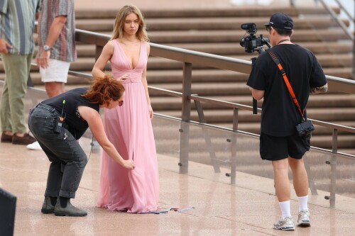 Sydney Sweeney with Glen Powell filming scenes for their upcoming untitled film in Sydney, Australia - March 27 2023

Sydney Sweeney Embraces Rom-Com Dressing in Flowy Pink Dress & Sparkling Sandals While Filming With Glen Powell in Australia

Sydney Sweeney was seen on Monday at the steps of the Sydney Opera House in Sydney, filming for her unnamed upcoming rom-com alongside leading man Glen Powell.

Sweeney and Powell were seen on the steps of the well-known performance center in rom-com-ready ensembles. Powell, who has previously starred in romantic features like “Set It Up,” wore a classic black-and-white tuxedo with black leather point-toe oxfords.

Whereas Sweeney looked every bit the leading lady in a flowing, deeply-cut, deftly-wrapped pink gown with a gauzy overlay of fabric over the skirt. The actress wore her well-known blond locks in a center part and styled them into soft, romantic waves.

For shoes, Sweeney donned a pair of peep-toe silver stiletto heels. The style featured a glittery finish and a ankle-strap for extra security.

When she’s not on set, Sweeney can be seen rocking a variety of footwear styles from ladylike mules to sky-high stilettos. She has been seen wearing a variety of designers, from Jimmy Choo to Tory Burch. Sweeney has been a Tory Burch brand ambassador since Apr. 2022, notably starring in the designer’s summer 2022 campaign, highlighting her popular Miller sandal line.

Sweeney has gained worldwide recognition after playing the love-obsessed Cassie on the hit HBO series “Euphoria”, and in the past year has been stepping into a variety of roles outside of the dramatic high school archetype.

On Jan. 11, Deadline reported that Sweeney and Powell signed on to star in a to-be-named rated-R romantic comedy film directed by Will Gluck. Not only is Sweeney the leading lady of the film, but she is also serving as the project’s executive producer.