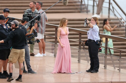 Sydney Sweeney with Glen Powell filming scenes for their upcoming untitled film in Sydney, Australia - March 27 2023

Sydney Sweeney Embraces Rom-Com Dressing in Flowy Pink Dress & Sparkling Sandals While Filming With Glen Powell in Australia

Sydney Sweeney was seen on Monday at the steps of the Sydney Opera House in Sydney, filming for her unnamed upcoming rom-com alongside leading man Glen Powell.

Sweeney and Powell were seen on the steps of the well-known performance center in rom-com-ready ensembles. Powell, who has previously starred in romantic features like “Set It Up,” wore a classic black-and-white tuxedo with black leather point-toe oxfords.

Whereas Sweeney looked every bit the leading lady in a flowing, deeply-cut, deftly-wrapped pink gown with a gauzy overlay of fabric over the skirt. The actress wore her well-known blond locks in a center part and styled them into soft, romantic waves.

For shoes, Sweeney donned a pair of peep-toe silver stiletto heels. The style featured a glittery finish and a ankle-strap for extra security.

When she’s not on set, Sweeney can be seen rocking a variety of footwear styles from ladylike mules to sky-high stilettos. She has been seen wearing a variety of designers, from Jimmy Choo to Tory Burch. Sweeney has been a Tory Burch brand ambassador since Apr. 2022, notably starring in the designer’s summer 2022 campaign, highlighting her popular Miller sandal line.

Sweeney has gained worldwide recognition after playing the love-obsessed Cassie on the hit HBO series “Euphoria”, and in the past year has been stepping into a variety of roles outside of the dramatic high school archetype.

On Jan. 11, Deadline reported that Sweeney and Powell signed on to star in a to-be-named rated-R romantic comedy film directed by Will Gluck. Not only is Sweeney the leading lady of the film, but she is also serving as the project’s executive producer.