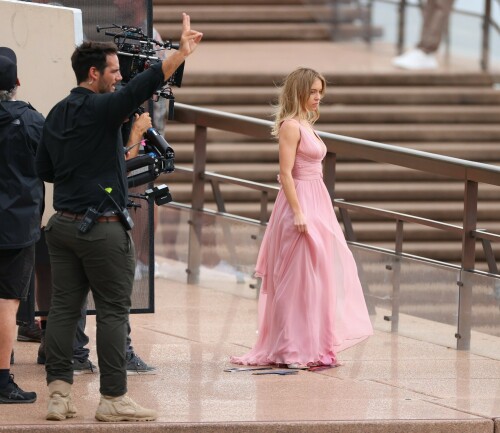 Sydney Sweeney with Glen Powell filming scenes for their upcoming untitled film in Sydney, Australia - March 27 2023

Sydney Sweeney Embraces Rom-Com Dressing in Flowy Pink Dress & Sparkling Sandals While Filming With Glen Powell in Australia

Sydney Sweeney was seen on Monday at the steps of the Sydney Opera House in Sydney, filming for her unnamed upcoming rom-com alongside leading man Glen Powell.

Sweeney and Powell were seen on the steps of the well-known performance center in rom-com-ready ensembles. Powell, who has previously starred in romantic features like “Set It Up,” wore a classic black-and-white tuxedo with black leather point-toe oxfords.

Whereas Sweeney looked every bit the leading lady in a flowing, deeply-cut, deftly-wrapped pink gown with a gauzy overlay of fabric over the skirt. The actress wore her well-known blond locks in a center part and styled them into soft, romantic waves.

For shoes, Sweeney donned a pair of peep-toe silver stiletto heels. The style featured a glittery finish and a ankle-strap for extra security.

When she’s not on set, Sweeney can be seen rocking a variety of footwear styles from ladylike mules to sky-high stilettos. She has been seen wearing a variety of designers, from Jimmy Choo to Tory Burch. Sweeney has been a Tory Burch brand ambassador since Apr. 2022, notably starring in the designer’s summer 2022 campaign, highlighting her popular Miller sandal line.

Sweeney has gained worldwide recognition after playing the love-obsessed Cassie on the hit HBO series “Euphoria”, and in the past year has been stepping into a variety of roles outside of the dramatic high school archetype.

On Jan. 11, Deadline reported that Sweeney and Powell signed on to star in a to-be-named rated-R romantic comedy film directed by Will Gluck. Not only is Sweeney the leading lady of the film, but she is also serving as the project’s executive producer.