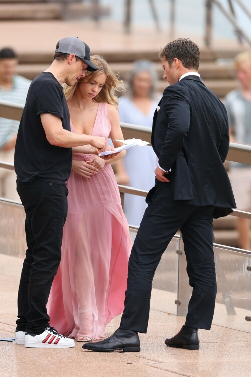 Sydney Sweeney with Glen Powell filming scenes for their upcoming untitled film in Sydney, Australia - March 27 2023

Sydney Sweeney Embraces Rom-Com Dressing in Flowy Pink Dress & Sparkling Sandals While Filming With Glen Powell in Australia

Sydney Sweeney was seen on Monday at the steps of the Sydney Opera House in Sydney, filming for her unnamed upcoming rom-com alongside leading man Glen Powell.

Sweeney and Powell were seen on the steps of the well-known performance center in rom-com-ready ensembles. Powell, who has previously starred in romantic features like “Set It Up,” wore a classic black-and-white tuxedo with black leather point-toe oxfords.

Whereas Sweeney looked every bit the leading lady in a flowing, deeply-cut, deftly-wrapped pink gown with a gauzy overlay of fabric over the skirt. The actress wore her well-known blond locks in a center part and styled them into soft, romantic waves.

For shoes, Sweeney donned a pair of peep-toe silver stiletto heels. The style featured a glittery finish and a ankle-strap for extra security.

When she’s not on set, Sweeney can be seen rocking a variety of footwear styles from ladylike mules to sky-high stilettos. She has been seen wearing a variety of designers, from Jimmy Choo to Tory Burch. Sweeney has been a Tory Burch brand ambassador since Apr. 2022, notably starring in the designer’s summer 2022 campaign, highlighting her popular Miller sandal line.

Sweeney has gained worldwide recognition after playing the love-obsessed Cassie on the hit HBO series “Euphoria”, and in the past year has been stepping into a variety of roles outside of the dramatic high school archetype.

On Jan. 11, Deadline reported that Sweeney and Powell signed on to star in a to-be-named rated-R romantic comedy film directed by Will Gluck. Not only is Sweeney the leading lady of the film, but she is also serving as the project’s executive producer.