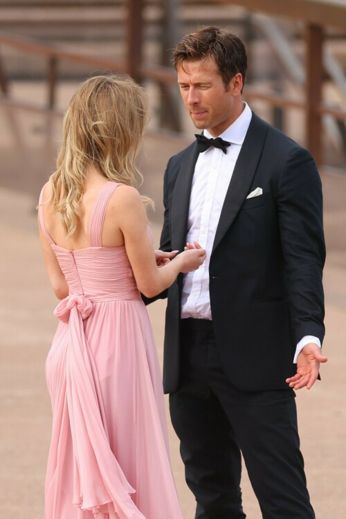 Sydney Sweeney with Glen Powell filming scenes for their upcoming untitled film in Sydney, Australia - March 27 2023

Sydney Sweeney Embraces Rom-Com Dressing in Flowy Pink Dress & Sparkling Sandals While Filming With Glen Powell in Australia

Sydney Sweeney was seen on Monday at the steps of the Sydney Opera House in Sydney, filming for her unnamed upcoming rom-com alongside leading man Glen Powell.

Sweeney and Powell were seen on the steps of the well-known performance center in rom-com-ready ensembles. Powell, who has previously starred in romantic features like “Set It Up,” wore a classic black-and-white tuxedo with black leather point-toe oxfords.

Whereas Sweeney looked every bit the leading lady in a flowing, deeply-cut, deftly-wrapped pink gown with a gauzy overlay of fabric over the skirt. The actress wore her well-known blond locks in a center part and styled them into soft, romantic waves.

For shoes, Sweeney donned a pair of peep-toe silver stiletto heels. The style featured a glittery finish and a ankle-strap for extra security.

When she’s not on set, Sweeney can be seen rocking a variety of footwear styles from ladylike mules to sky-high stilettos. She has been seen wearing a variety of designers, from Jimmy Choo to Tory Burch. Sweeney has been a Tory Burch brand ambassador since Apr. 2022, notably starring in the designer’s summer 2022 campaign, highlighting her popular Miller sandal line.

Sweeney has gained worldwide recognition after playing the love-obsessed Cassie on the hit HBO series “Euphoria”, and in the past year has been stepping into a variety of roles outside of the dramatic high school archetype.

On Jan. 11, Deadline reported that Sweeney and Powell signed on to star in a to-be-named rated-R romantic comedy film directed by Will Gluck. Not only is Sweeney the leading lady of the film, but she is also serving as the project’s executive producer.