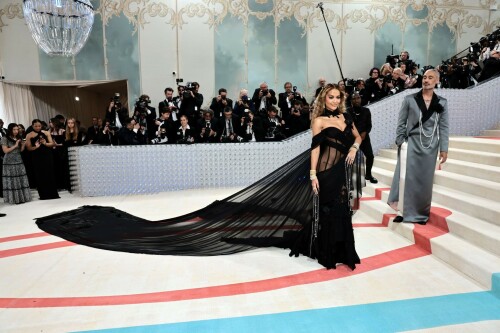 Rita Ora Makes a Case for Sheer on Met Gala Red Carpet 2023 in Prabal Gurung Dress & Strappy Sandals With Taika Waititi

Rita Ora arrived at the 2023 Met Gala in New York wearing an all-black ensemble. The singer posed on the carpet with her husband, director Taika Waititi.

Ora donned a daring outfit that featured detailed draping, striking cutouts and well-defined boning from Prabal Gurung.

The Nepalese-American fashion designer has been a fixture at the Met Gala since 2010. His designs have graced the red carpet, showcasing his signature style that often combines traditional Nepalese influences with modern, edgy elements. He has dressed a range of celebrities, from Sarah Jessica Parker to Zendaya over the years.

Regarding her footwear choice, Ora strapped on a pair of strappy sandals with a generous platform. These strappy platform sandals feature a chic ankle buckle closure that provides a secure fit. The almond toe design adds a touch of elegance, while the 6-inch heel elongates the legs and creates a flattering silhouette.

Ora’s fashion style is a mix of edgy and glamorous, often pushing boundaries with bold statement pieces. She is known for wearing daring outfits that showcase her confident and daring personality. Rita has also been a standout at the Met Gala, consistently impressing with her unique and avant-garde choices. From her bold silver feathered gown in 2016 to her Prada moment in 2021, she always manages to turn heads on the red carpet.

The Met Gala raises funds for the Metropolitan Museum of Art in New York City and celebrates the Costume Institute’s annual exhibits. This year’s theme, “Karl Lagerfeld: A Line of Beauty,” celebrates the life and career of designer Karl Lagerfeld. The 2023 event is notably co-chaired by Dua Lipa, Roger Federer, Michaela Coel, Penelope Cruz and Vogue editor-in-chief Anna Wintour.

Rita Ora attends The 2023 Met Gala Celebrating "Karl Lagerfeld: A Line Of Beauty" at The Metropolitan Museum of Art on May 01, 2023 in New York City.

Met Gala 2023: Rita Ora sizzles in a black sheer gown as she joins dapper husband Taika Waititi on the star-studded red carpet.

Rita Ora brought the goth glamour to the Met Gala 2023 red carpet with a sheer corseted gown by Prabal Gurung.

#RitaOra #2023MetGala