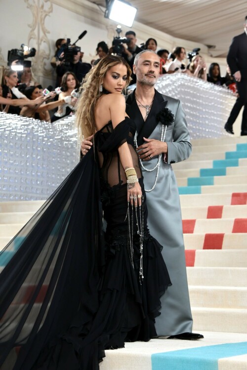 Rita Ora Makes a Case for Sheer on Met Gala Red Carpet 2023 in Prabal Gurung Dress & Strappy Sandals With Taika Waititi

Rita Ora arrived at the 2023 Met Gala in New York wearing an all-black ensemble. The singer posed on the carpet with her husband, director Taika Waititi.

Ora donned a daring outfit that featured detailed draping, striking cutouts and well-defined boning from Prabal Gurung.

The Nepalese-American fashion designer has been a fixture at the Met Gala since 2010. His designs have graced the red carpet, showcasing his signature style that often combines traditional Nepalese influences with modern, edgy elements. He has dressed a range of celebrities, from Sarah Jessica Parker to Zendaya over the years.

Regarding her footwear choice, Ora strapped on a pair of strappy sandals with a generous platform. These strappy platform sandals feature a chic ankle buckle closure that provides a secure fit. The almond toe design adds a touch of elegance, while the 6-inch heel elongates the legs and creates a flattering silhouette.

Ora’s fashion style is a mix of edgy and glamorous, often pushing boundaries with bold statement pieces. She is known for wearing daring outfits that showcase her confident and daring personality. Rita has also been a standout at the Met Gala, consistently impressing with her unique and avant-garde choices. From her bold silver feathered gown in 2016 to her Prada moment in 2021, she always manages to turn heads on the red carpet.

The Met Gala raises funds for the Metropolitan Museum of Art in New York City and celebrates the Costume Institute’s annual exhibits. This year’s theme, “Karl Lagerfeld: A Line of Beauty,” celebrates the life and career of designer Karl Lagerfeld. The 2023 event is notably co-chaired by Dua Lipa, Roger Federer, Michaela Coel, Penelope Cruz and Vogue editor-in-chief Anna Wintour.

Rita Ora attends The 2023 Met Gala Celebrating "Karl Lagerfeld: A Line Of Beauty" at The Metropolitan Museum of Art on May 01, 2023 in New York City.

Met Gala 2023: Rita Ora sizzles in a black sheer gown as she joins dapper husband Taika Waititi on the star-studded red carpet.

Rita Ora brought the goth glamour to the Met Gala 2023 red carpet with a sheer corseted gown by Prabal Gurung.

#RitaOra #2023MetGala