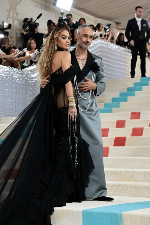 Met Gala 2023: Rita Ora Is Serving Fashion Witch at The Met Gala

May shmay! It's spooky season for Rita.

Fifty Shades of Grey actor Rita Ora arrived at the 2023 Met Gala in a witchy and bewitching gown that makes us feel incredibly October given that it's May. Is she vying for a part on her beau Taika Waititi's What We Do in the Shadows? Very much still in her boudoir fashion era. It's not not lingerie.

Ora's Prabal Gurung gown for the event plays with sheer and with layers, two elements she's been wearing a lot lately, but it's the nails and train that really stand out. Her long black…cloak? Cape? Scarf? covered nearly the length of the blue, white, and red carpet, creating a dramatic silhouette and, frankly, giving her a moment to get all camera lenses on her.

Equally decadent were the jewels literally dripping from her fingertips, as glittering ropes cascaded from her nails. Okay but like, how's she gonna eat dinner inside?

The smoky eye will never die. But combined with the lined lips? It's the new classics.

Ora reflected on the night's theme—"Karl Lagerfeld: A Line of Beauty"—on Instagram, sharing two posts in honor of the late designer. In the first, she and Lagerfeld pose together at various events, she walks the runway in a silver ensemble, and wears his designs for Chanel in various shoots.

In the second photo roundup, seemingly taken recently (peep the nails), Ora plays around in an old costume made by Karl himself. "In memory of Karl I had to bring back this custom piece he made me for a Chanel show performance I did with him in Monaco back in 2013. See you tomorrow!!" the singer wrote.

It's not that this doesn't go with the theme—the flowers and the black are totally Lagerfeldian—but anyone else think this is what she would have worn no matter what?

Rita Ora attends The 2023 Met Gala Celebrating "Karl Lagerfeld: A Line Of Beauty" at The Metropolitan Museum of Art on May 01, 2023 in New York City.

Met Gala 2023: Rita Ora sizzles in a black sheer gown as she joins dapper husband Taika Waititi on the star-studded red carpet.

Rita Ora brought the goth glamour to the Met Gala 2023 red carpet with a sheer corseted gown by Prabal Gurung.

#RitaOra #2023MetGala